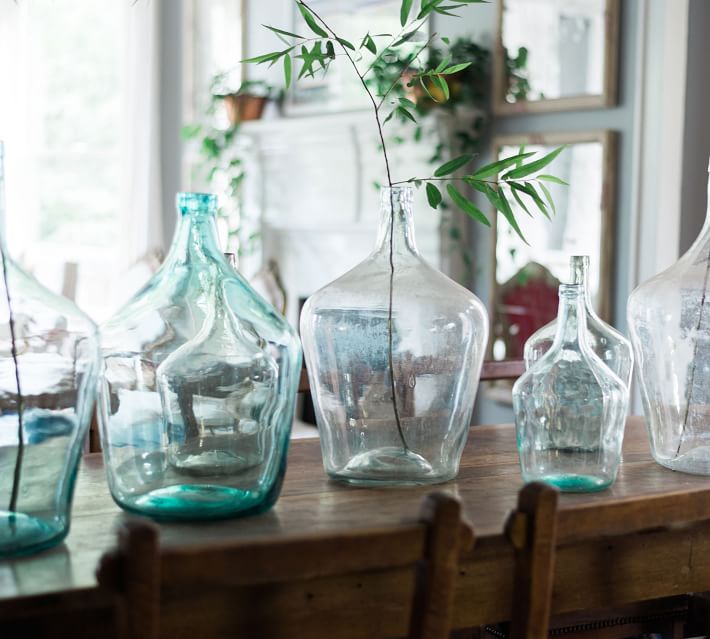 collection of blue and clear demijohns on a table one holding a single green stem