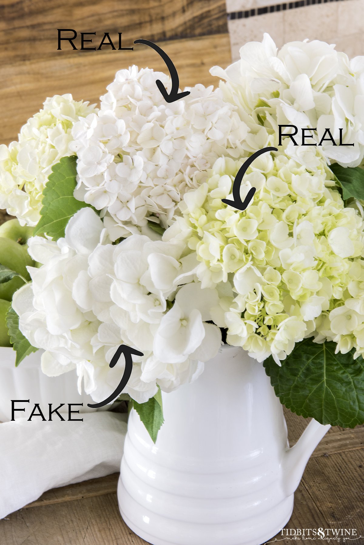 Closeup of white hydrangeas in a white pitcher with text overlay showing which are real and which are fake