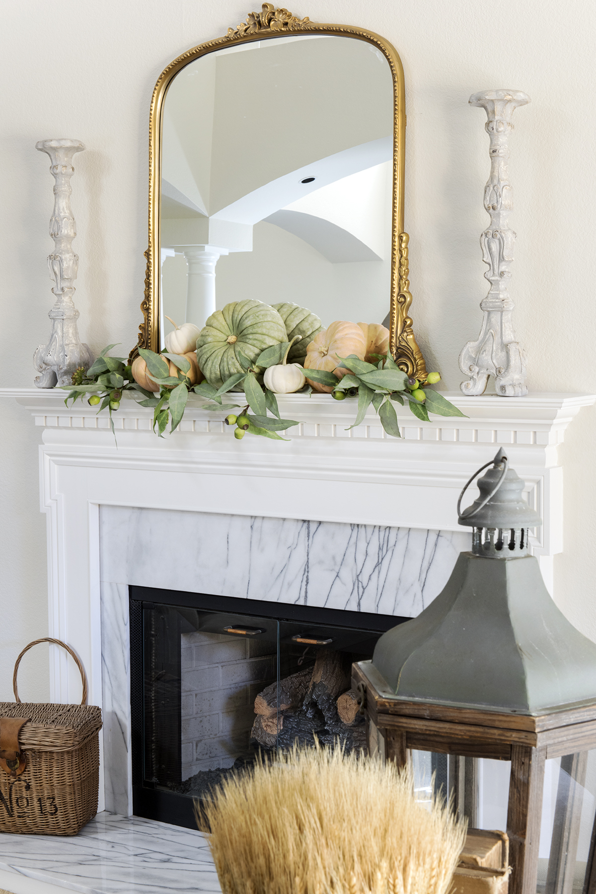 white fireplace with cararra marble decorated for fall with gold mirror and pumpkins and basket on hearth