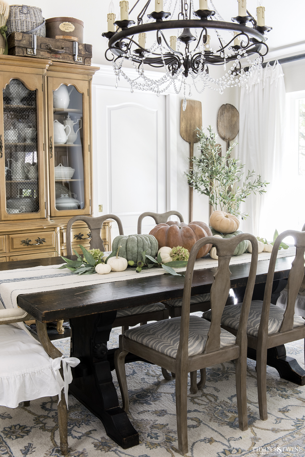 french dining room with gustavian wood chairs and orange green and white pumpkins on the trestle table and antique bread paddles on wall