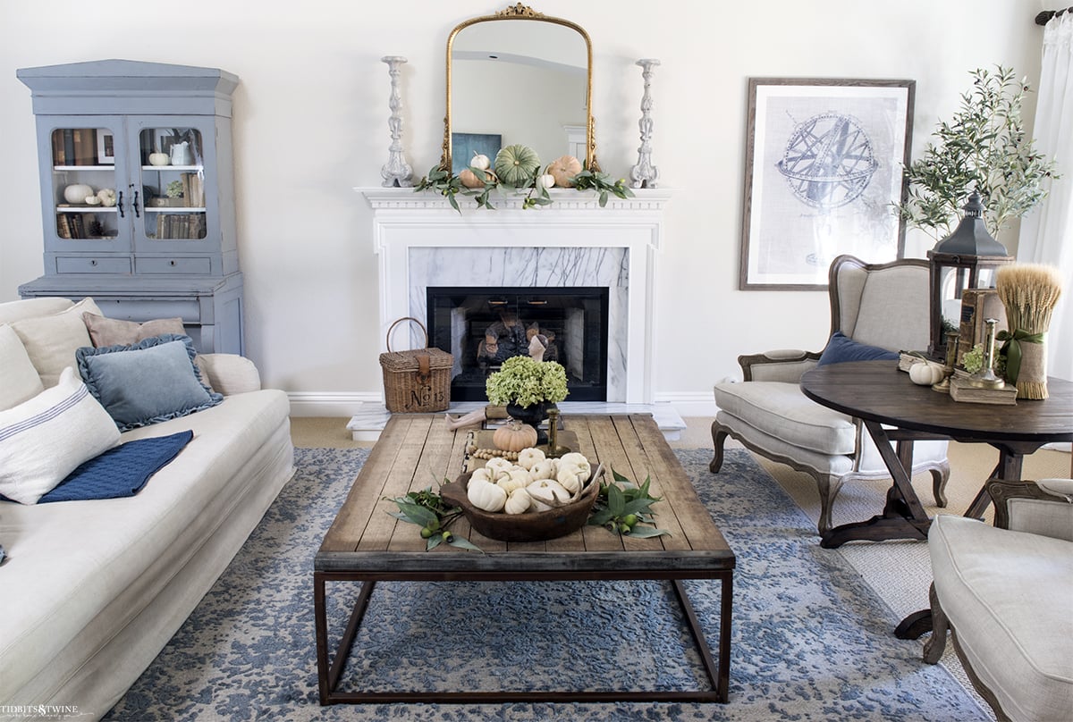 blue and white french living room with fireplace linen furniture and industrial coffee table decorated for fall with white pumpkins