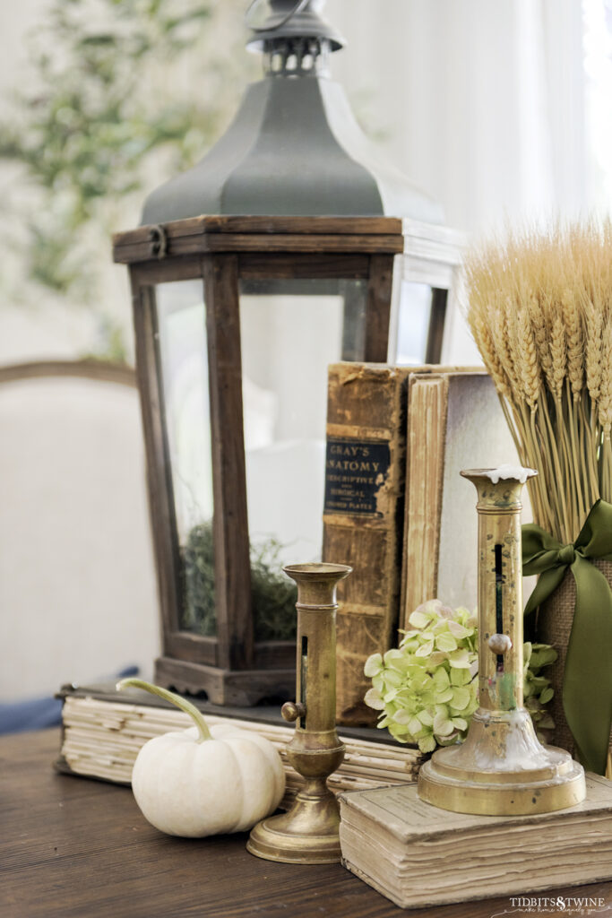 side table styled with wooden lantern old books brass candlesticks and wheat for fall