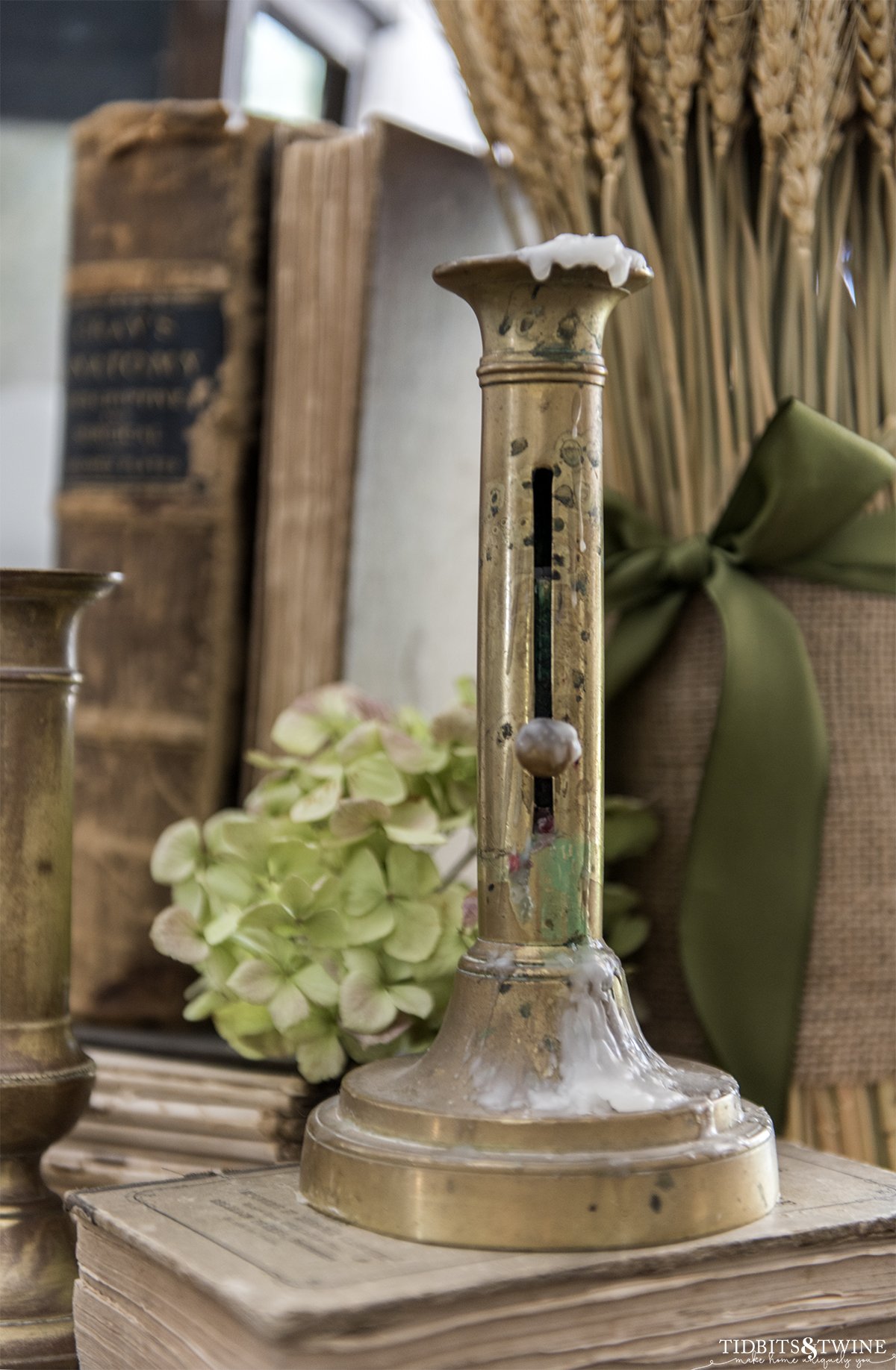 antique french brass candlestick sitting on old books with dried hydrangea and wheat bouquet in background