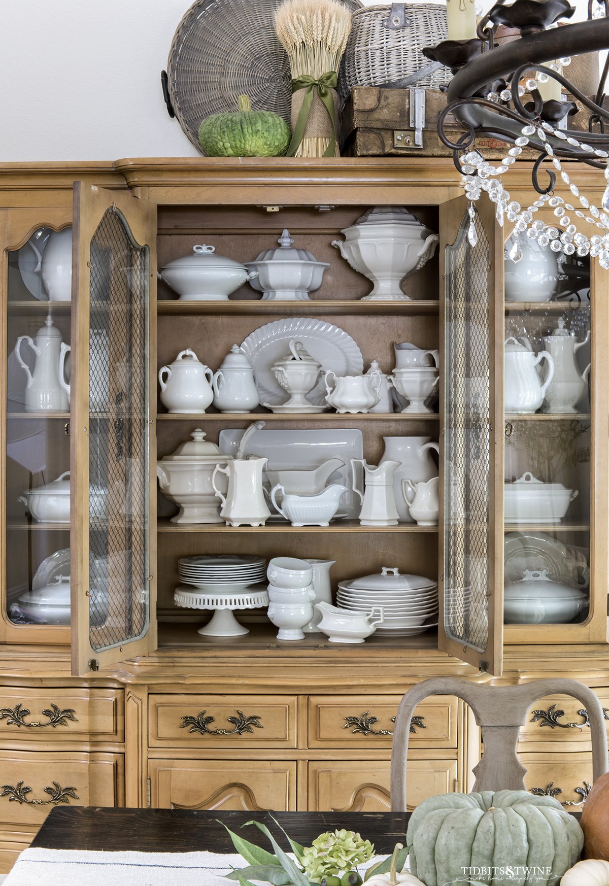 french cabinet full of antique white ironstone collection in a dining room decorated for fall with orange green and white pumpkins