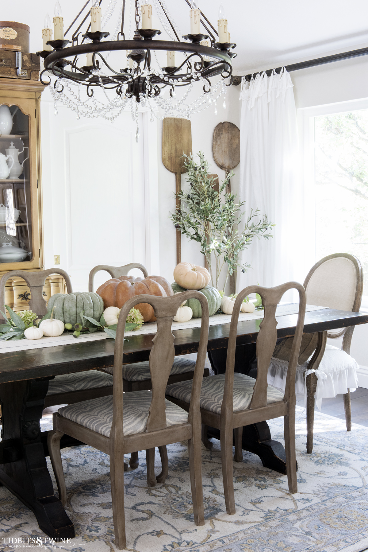 french dining room with gustavian wood chairs and orange green and white pumpkins on the trestle table and antique bread paddles on wall