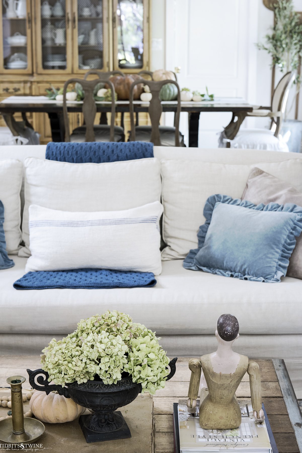 living room industrial coffee table with urn of dried hydrangea and santos doll with slipcovered sofa in background with blue cableknit throw