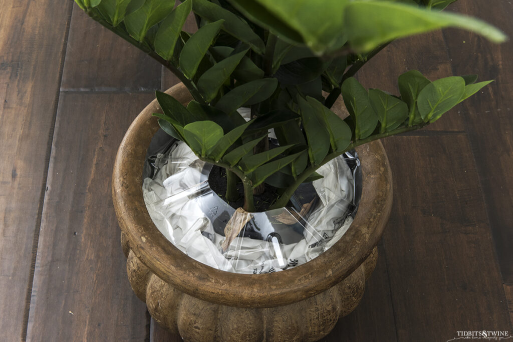 artificial zz plant in brown pot surrounded by stuffed grocery bags with clear tray on top