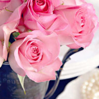 pink roses in an antique trophy with a plate holding a pearl necklace below