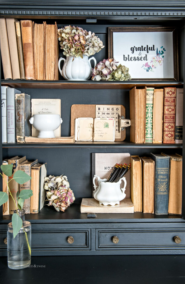 Black vintage cabinet decoratively styled with antique books dried hydrangea and ironstone