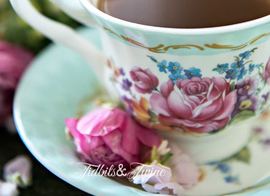 turquoise and pink antique teacup filled with coffee with pink flowers in the saucer and pink flowers in background