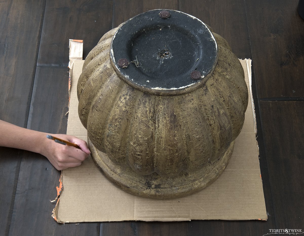 brown pot upside down on cardboard with hand tracing around the rim of pot