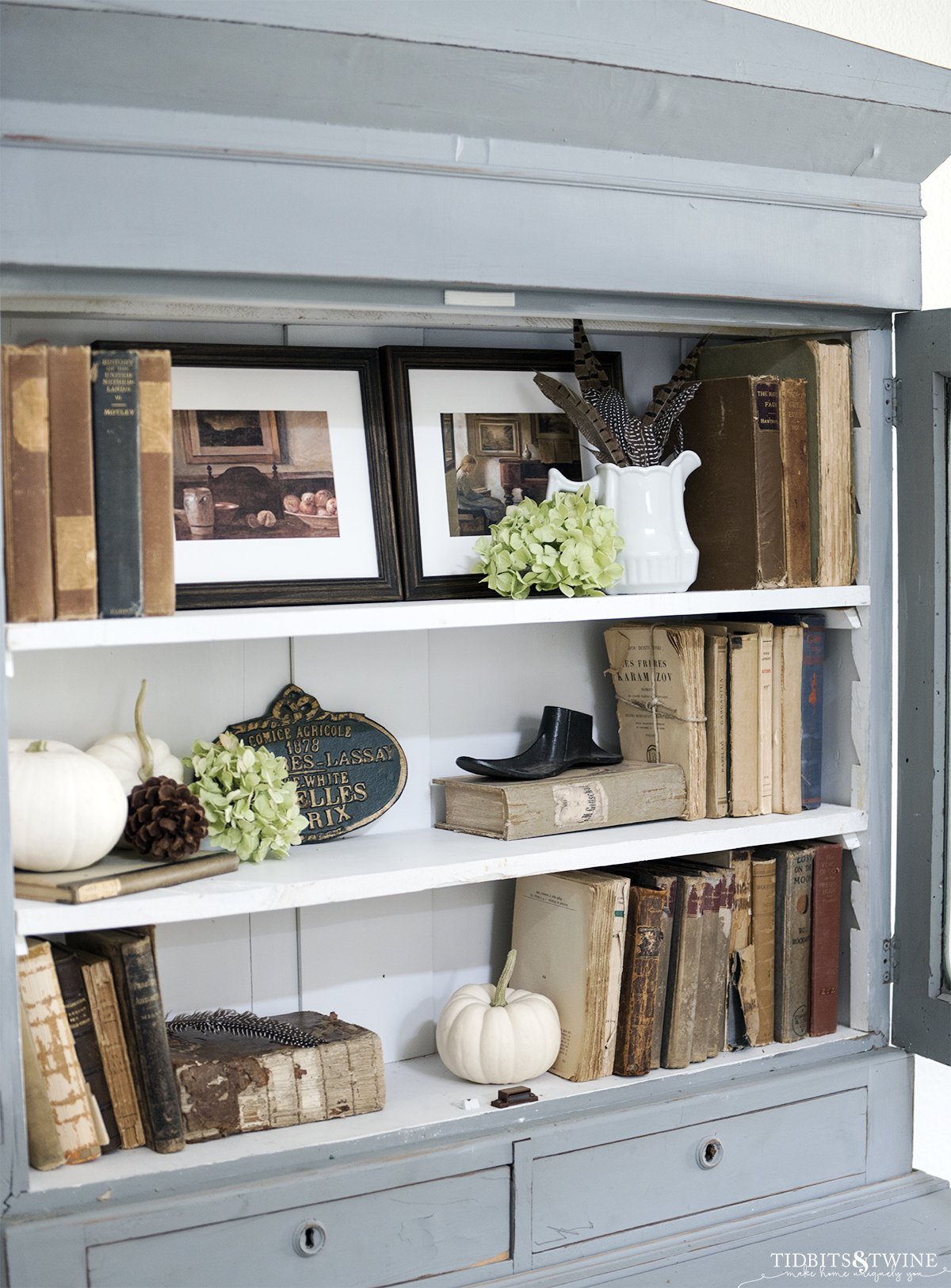 blue cabinet with white shelves decorated with antique books and white pumpkins art and dried hydrangea