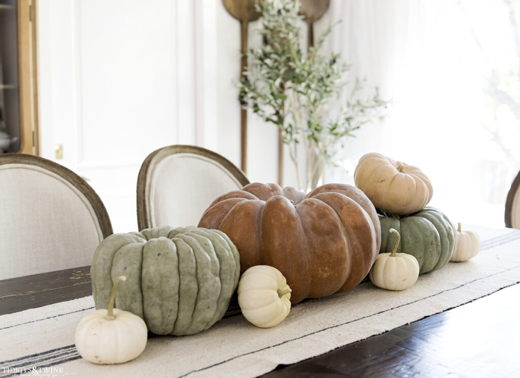 French dining room with terracotta pumpkin on center of table and smaller green ones on either side and white pumpkins scattered