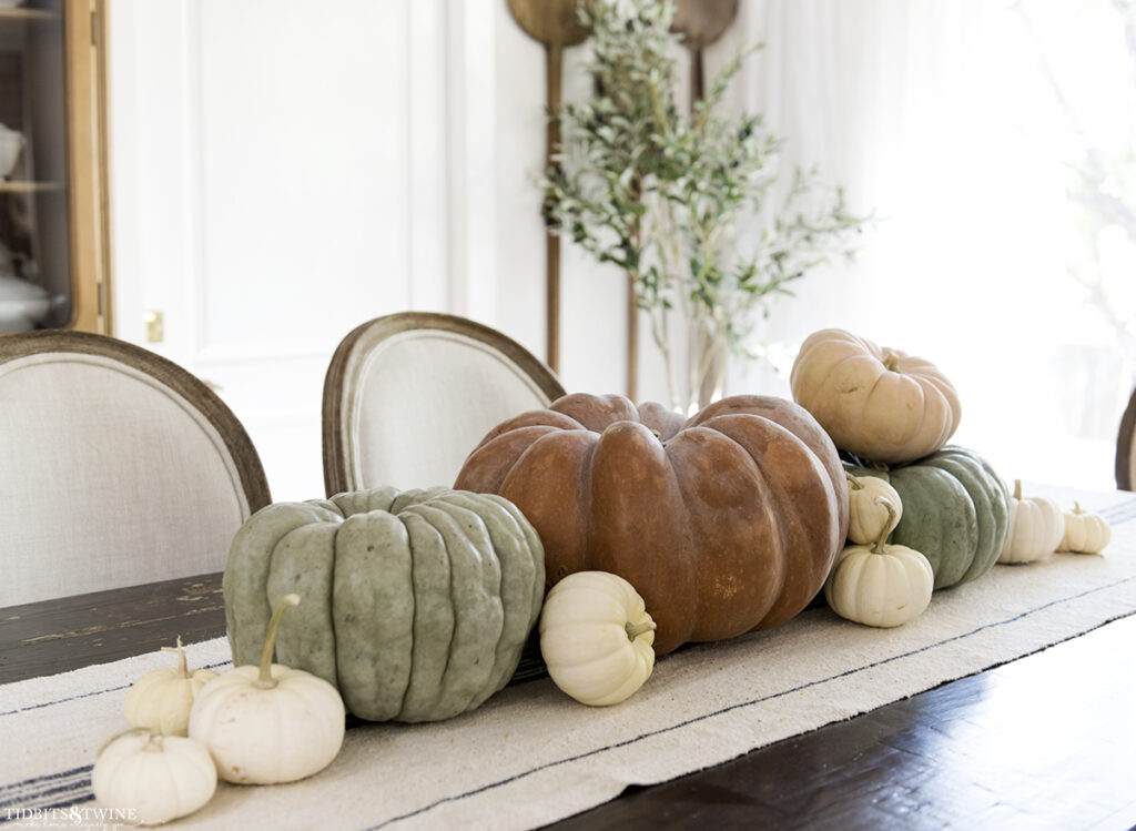 French dining room with terracotta pumpkin on center of table and smaller green ones on either side and white pumpkins scattered
