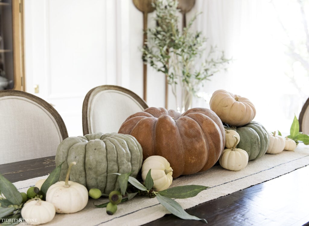 French dining room with terracotta pumpkin on center of table and smaller green ones on either side and white pumpkins scattered with eucalyptus