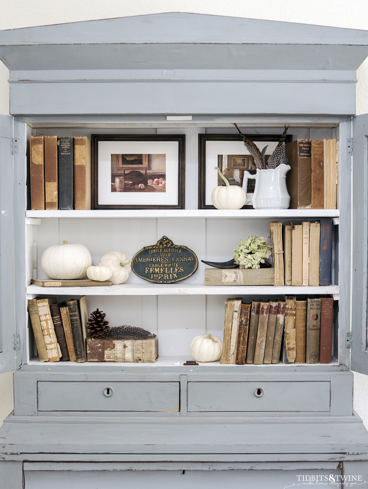 antique blue cabinet with three white shelves styled with old books pumpkins and hydrangea for fall