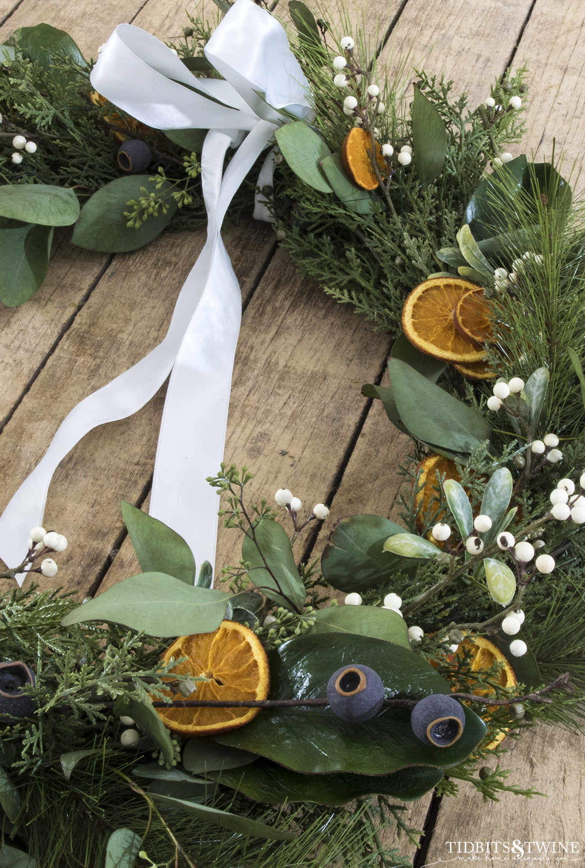 closeup of diy dried orange christmas wreath with greenery and berries and white ribbon bow