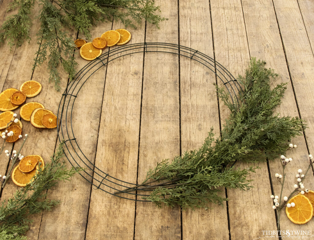 wire wreath frame on rustic table with some greenery being wired to it