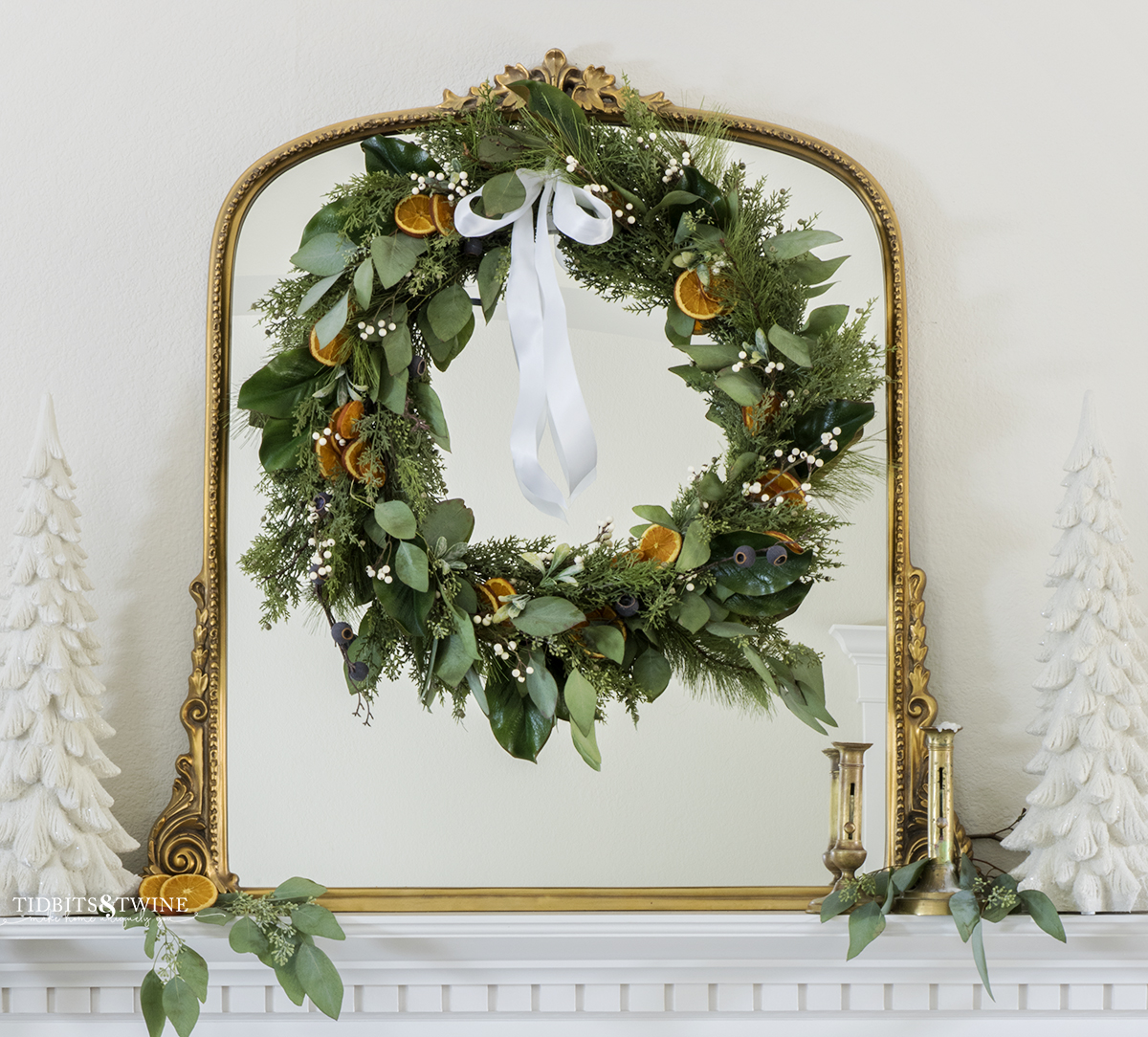 dried orange slice Christmas wreath with greenery and berries on a gold mantel above a fireplace
