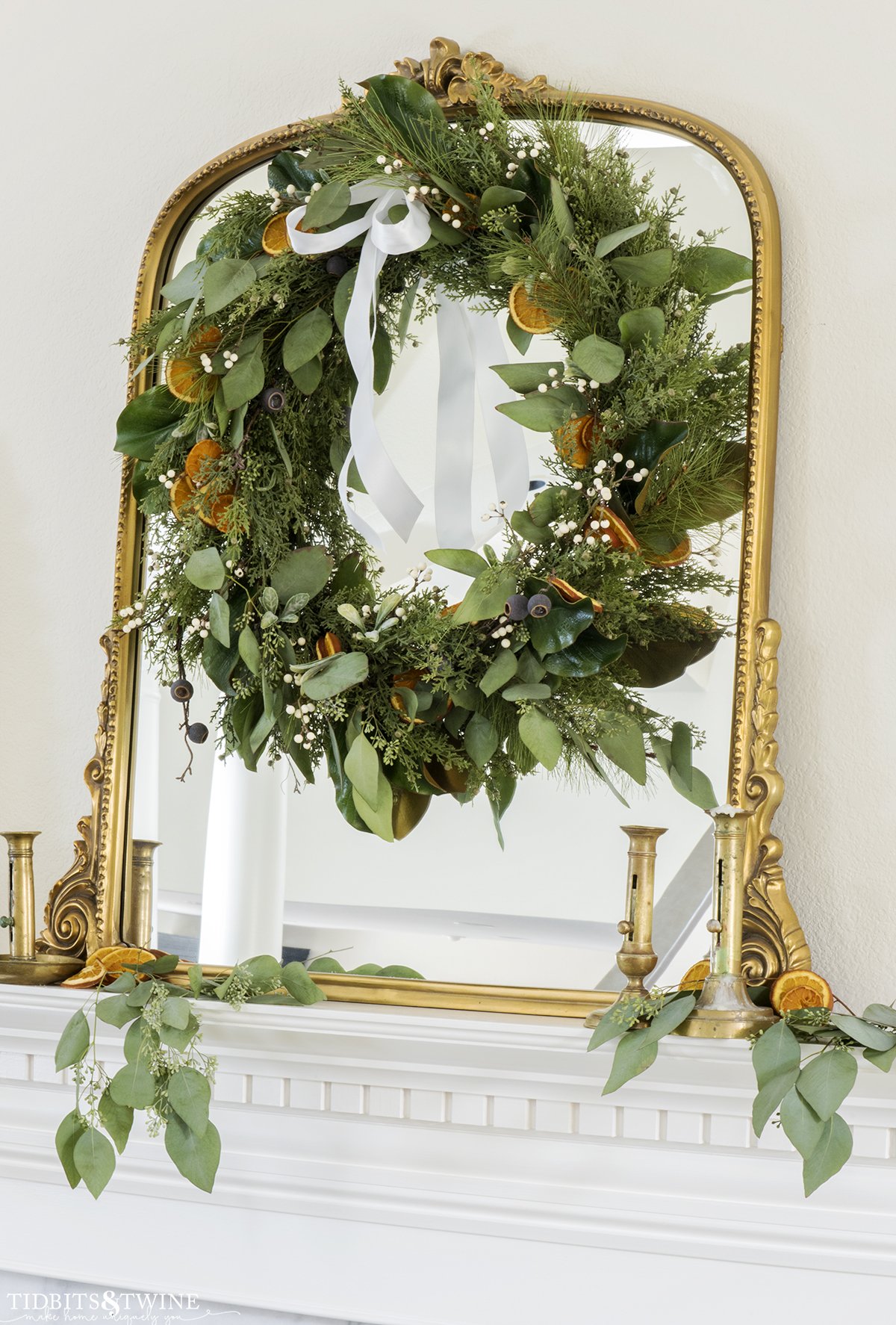 dried orange slice Christmas wreath with greenery and berries on a gold mantel above a fireplace