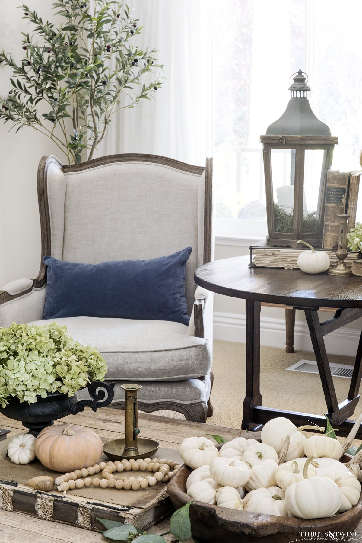 french wingback chair with blue pillow and antique wine tasting table on side and coffee table in front both decorated for fall