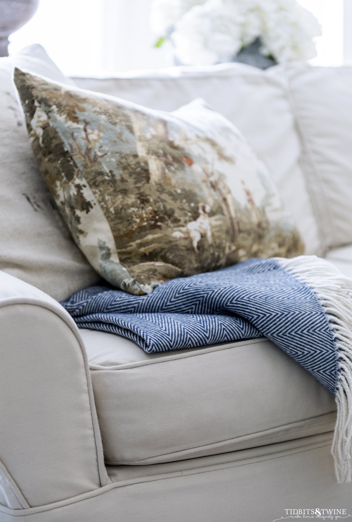 closeup of blue and white herringbone throw with white fringe showing how to fold on sofa with fall decorative pillow and grain sack pillow on top