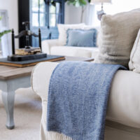 blue and white herringbone throw with white fringe folded over the arm of slipcovered sofa in living room