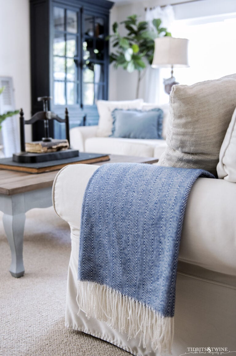 blue and white herringbone throw with white fringe folded over the arm of slipcovered sofa in living room
