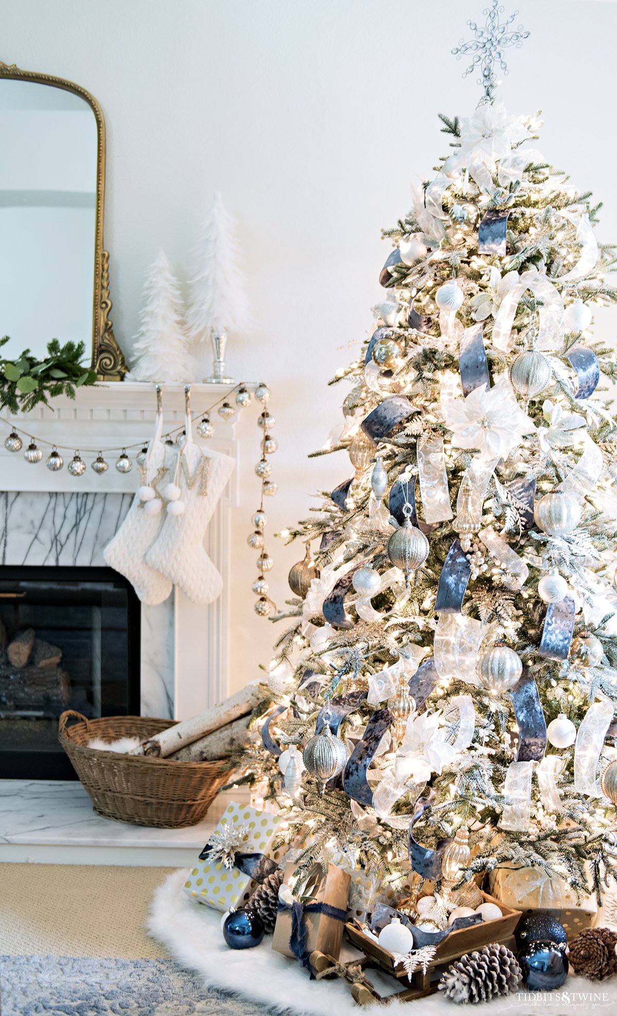 blue and white french christmas tree with fireplace mantel in background with white stockings and white feather trees