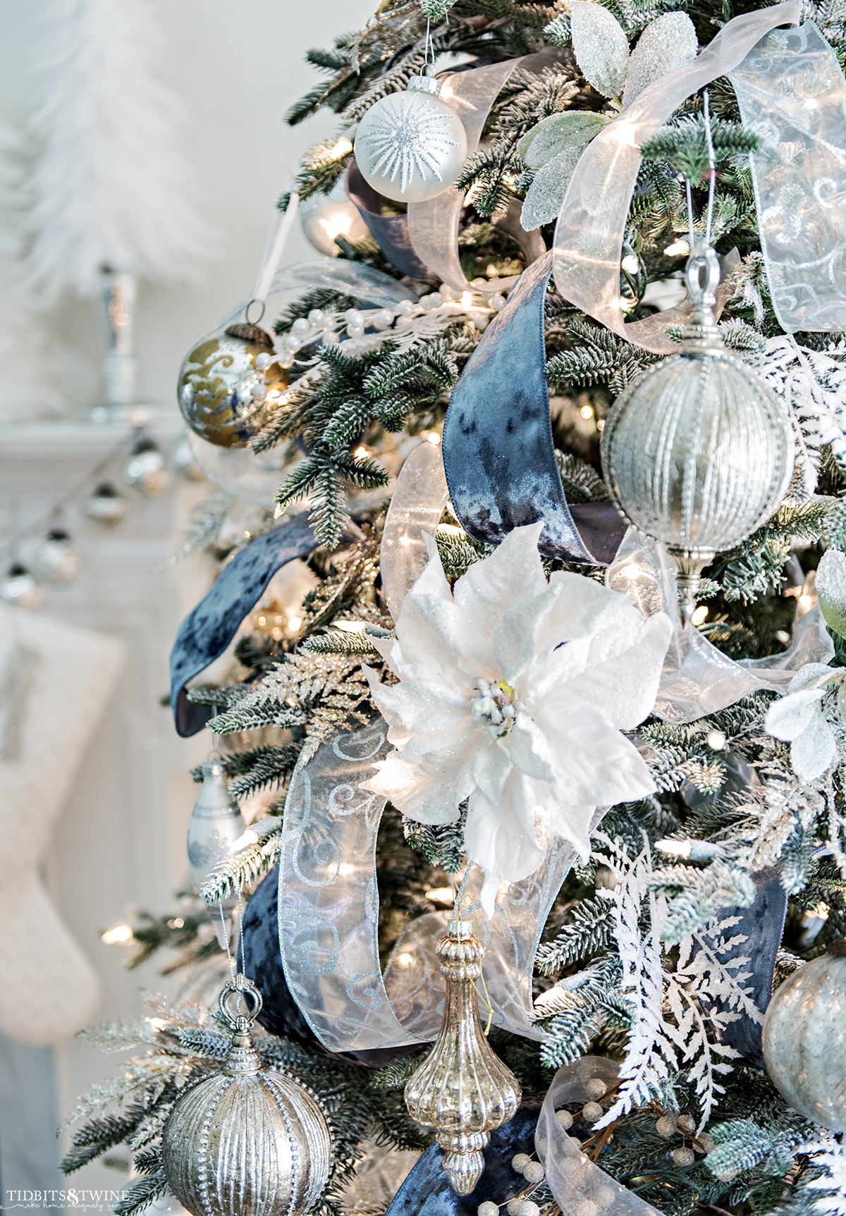 closeup of white poinsettia on christmas tree decorated with gold white and silver ornaments and blue ribbon