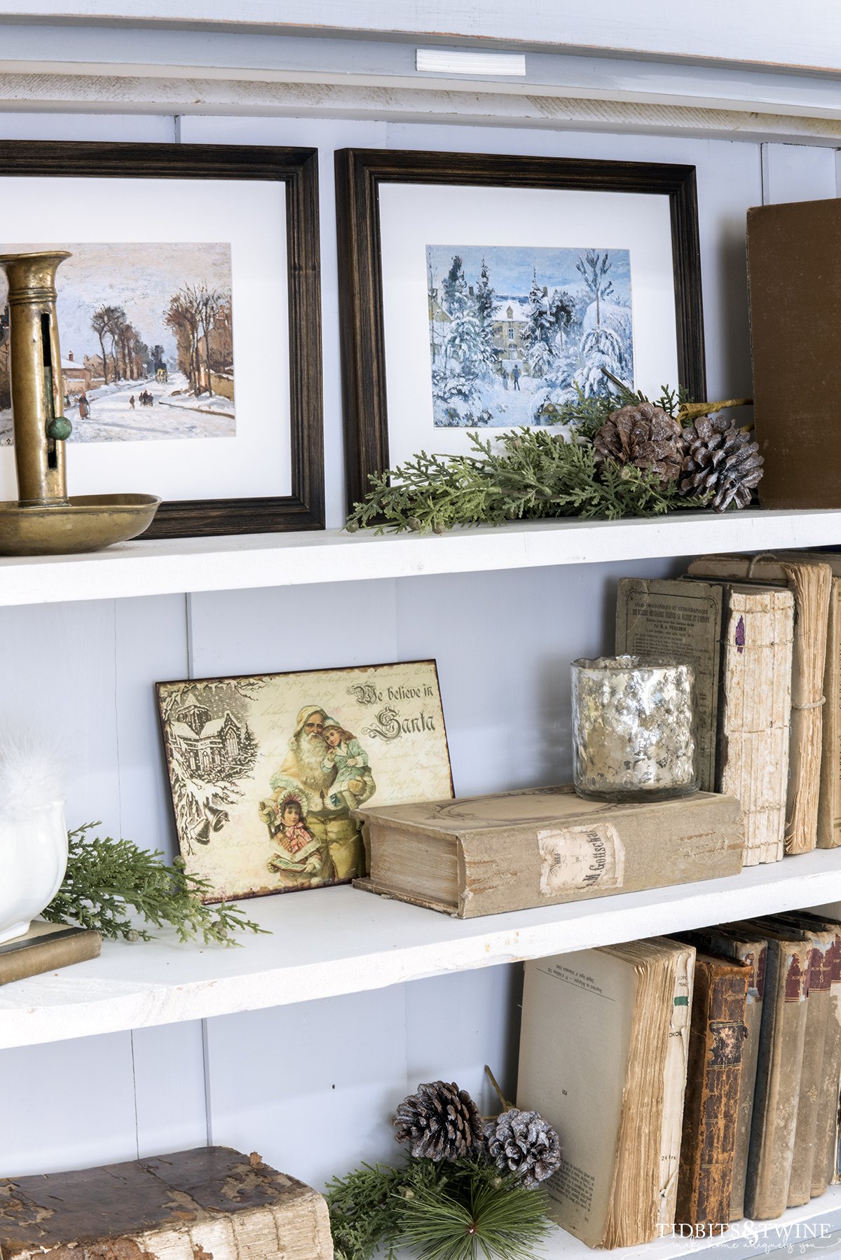 french blue cabinet with styled shelves holding antique books ironstone greenery and small winter framed art