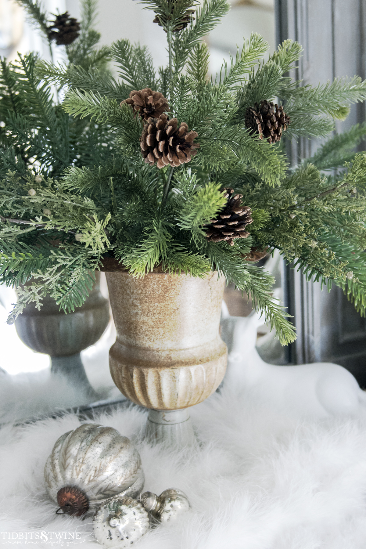 french urn filled with Christmas greenery with trumeau mirror behind and white snow at base