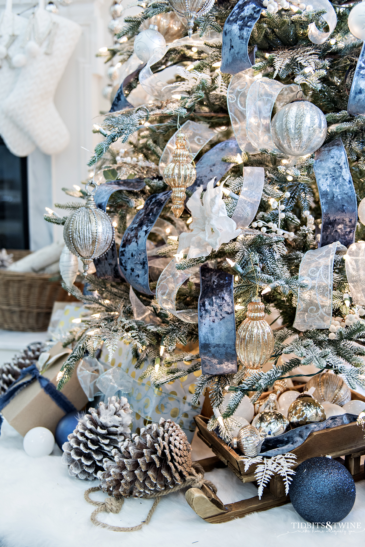 white and gold christmas presents under a flocked tree with ornaments and pinecones