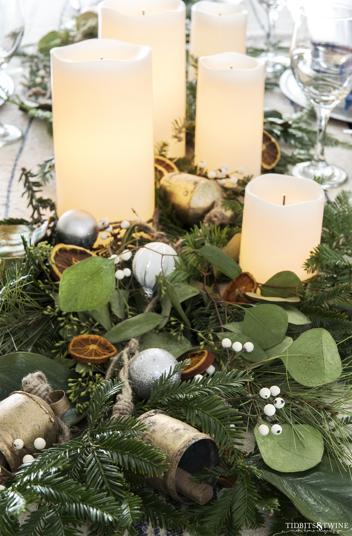 christmas centerpiece with greenery and orange slices bells and candles on a dining table