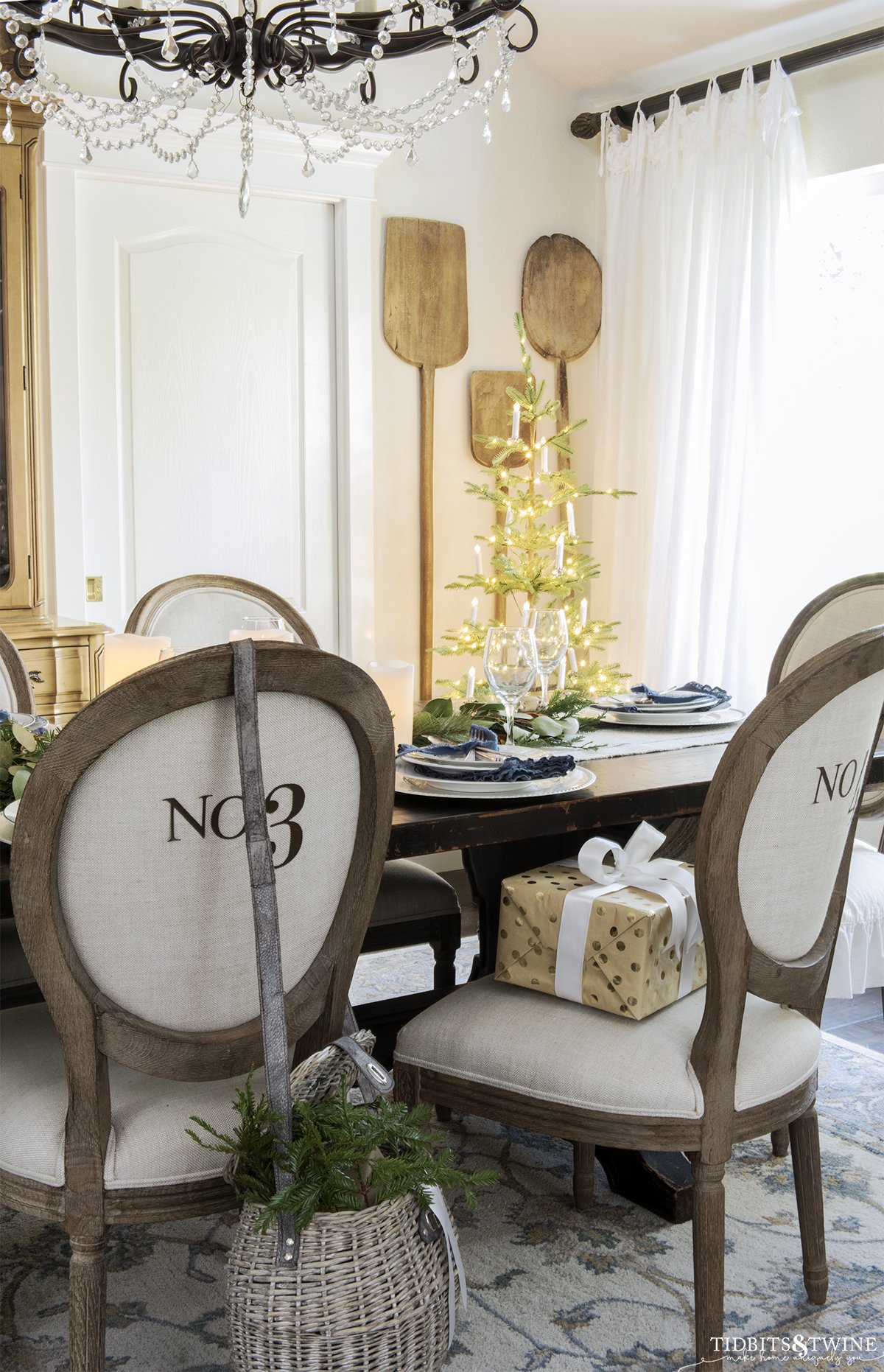 french christmas dining room with round linen chairs and small tree in corner lit with candles