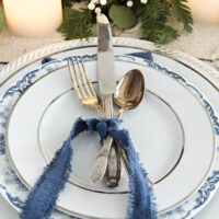 vintage flatware tied together with blue velvet ribbon on a silver rimmed white plate on top of blue and white transferware plate