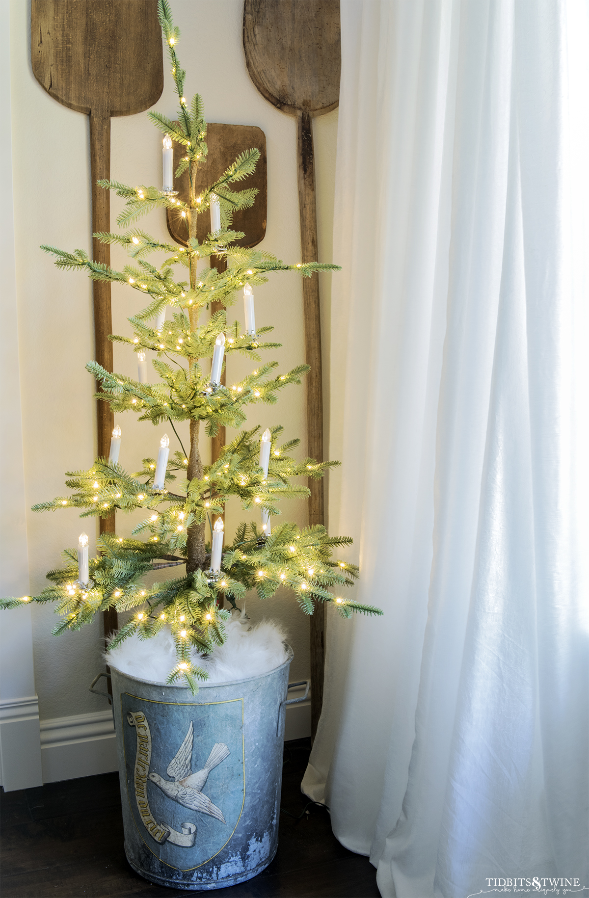 small sparse christmas tree in corner in an antique european bucket with white clip on candles and vintage bread paddles on the wall