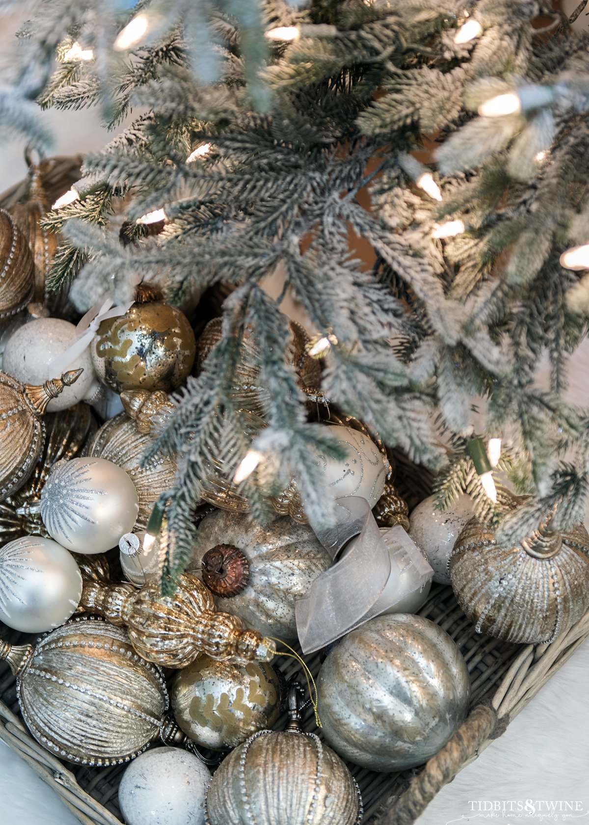 white silver and gold ornaments in a basket tray underneath a flocked christmas tree