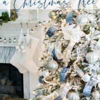 blue and white french christmas tree with fireplace mantel in background with white stockings and white feather trees