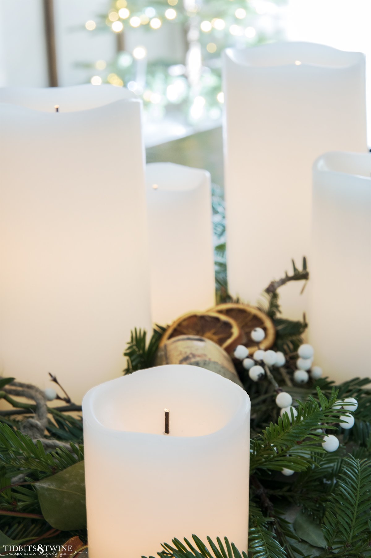 battery operated white candles in varying heights on a christmas table with greenery