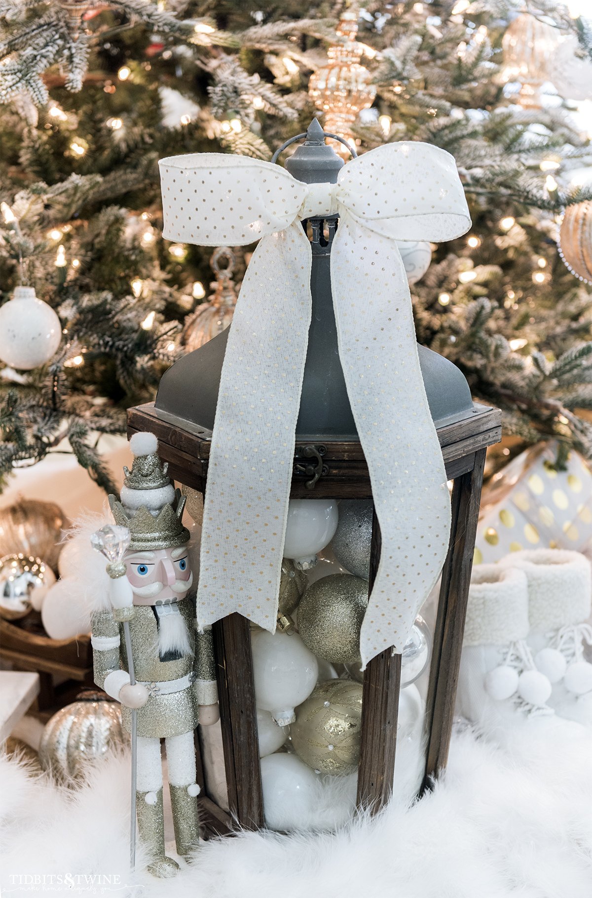 lantern filled with ornaments and a large bow on top in front of a Christmas tree