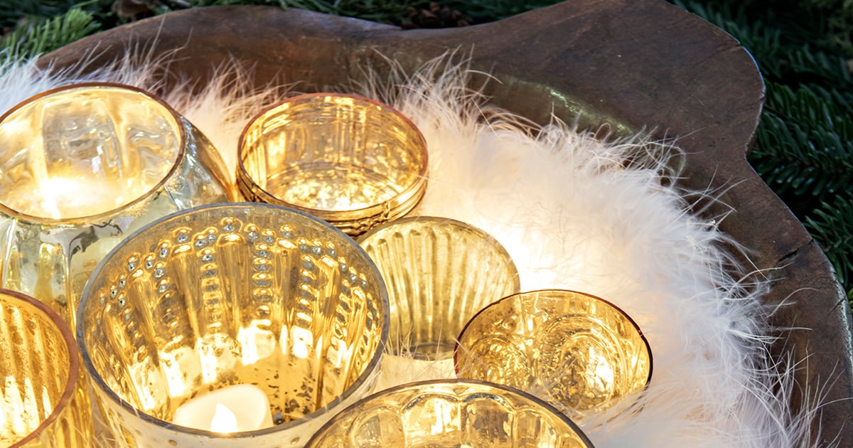 dough bowl full of glass votives with candles and a feather boa tucked around them with Christmas greens around bowl