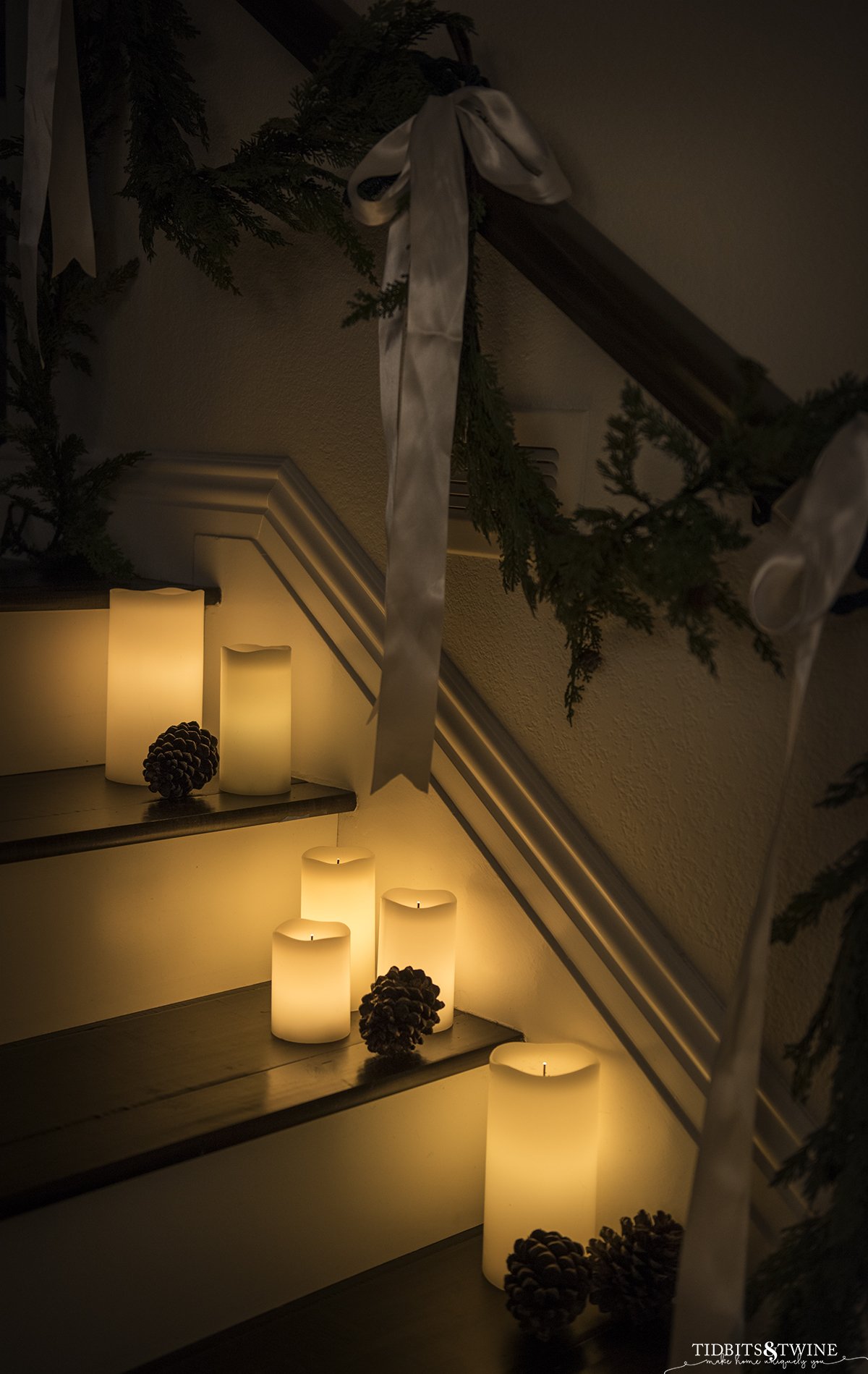 glowing candles on stairs with pinecones and evergreen garland on banister with white ribbon bows for winter decor