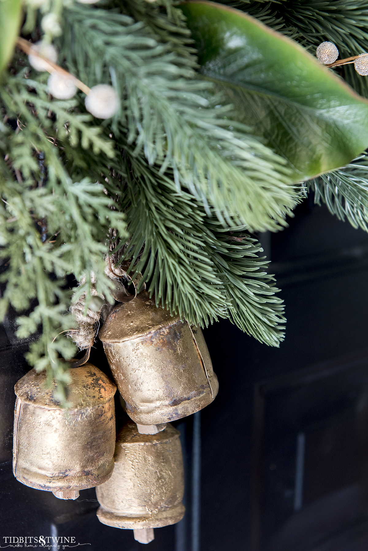 closeup of antique brass bells hanging from a christmas wreath on a black front door