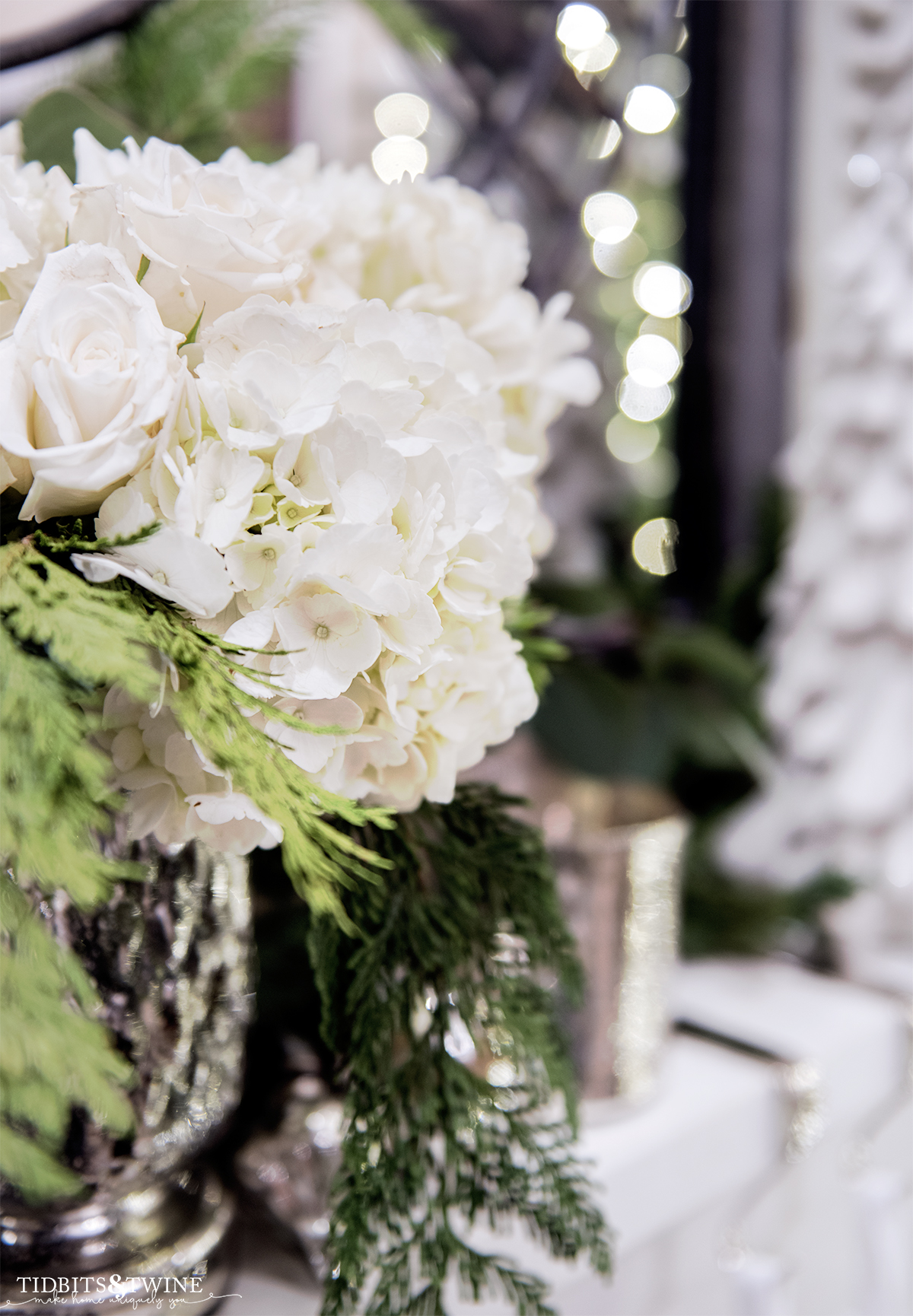 closeup of christmas floral arrangement with hydrangea white roses and christmas greenery in a mercury glass vase