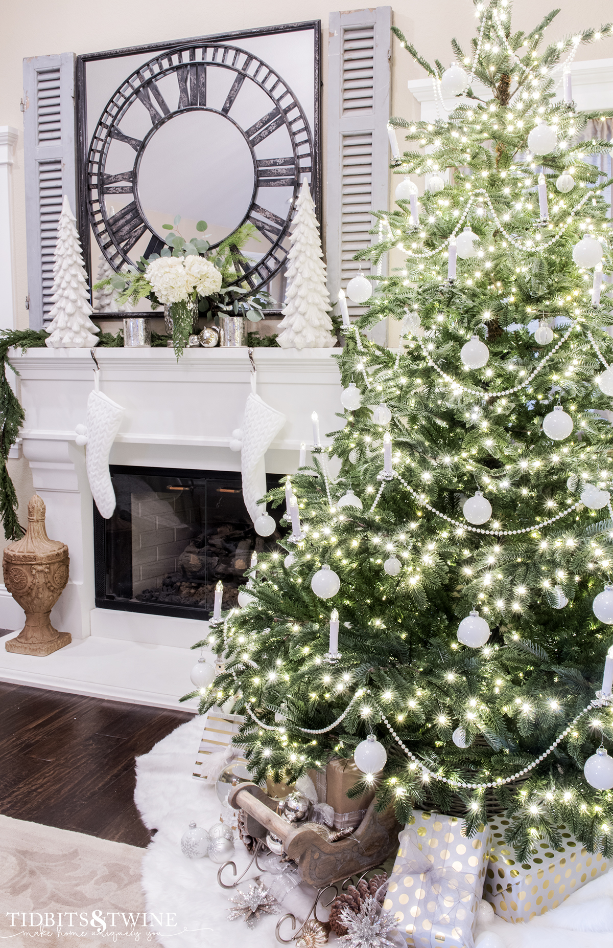 bedroom with european fir christmas tree decorated with white ornaments and candles next to a fireplace with blue shutters above mantel