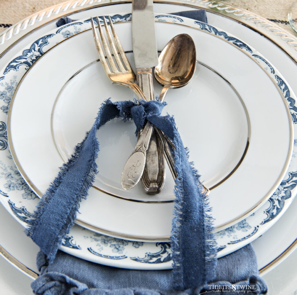 vintage flatware tied together with blue velvet ribbon on a silver rimmed white plate on top of blue and white transferware plate