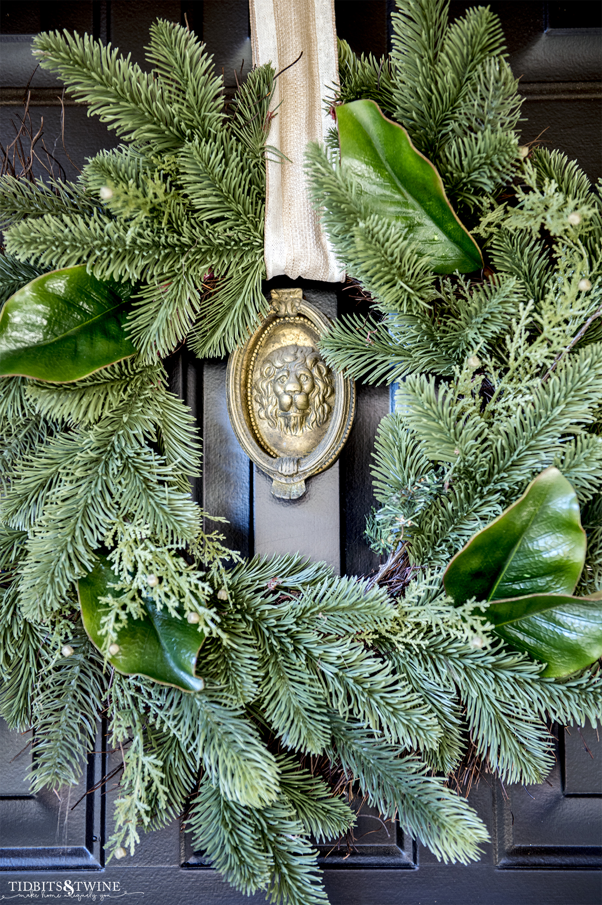 evergreen wreath on black front door with brass lionhead door knocker in the center