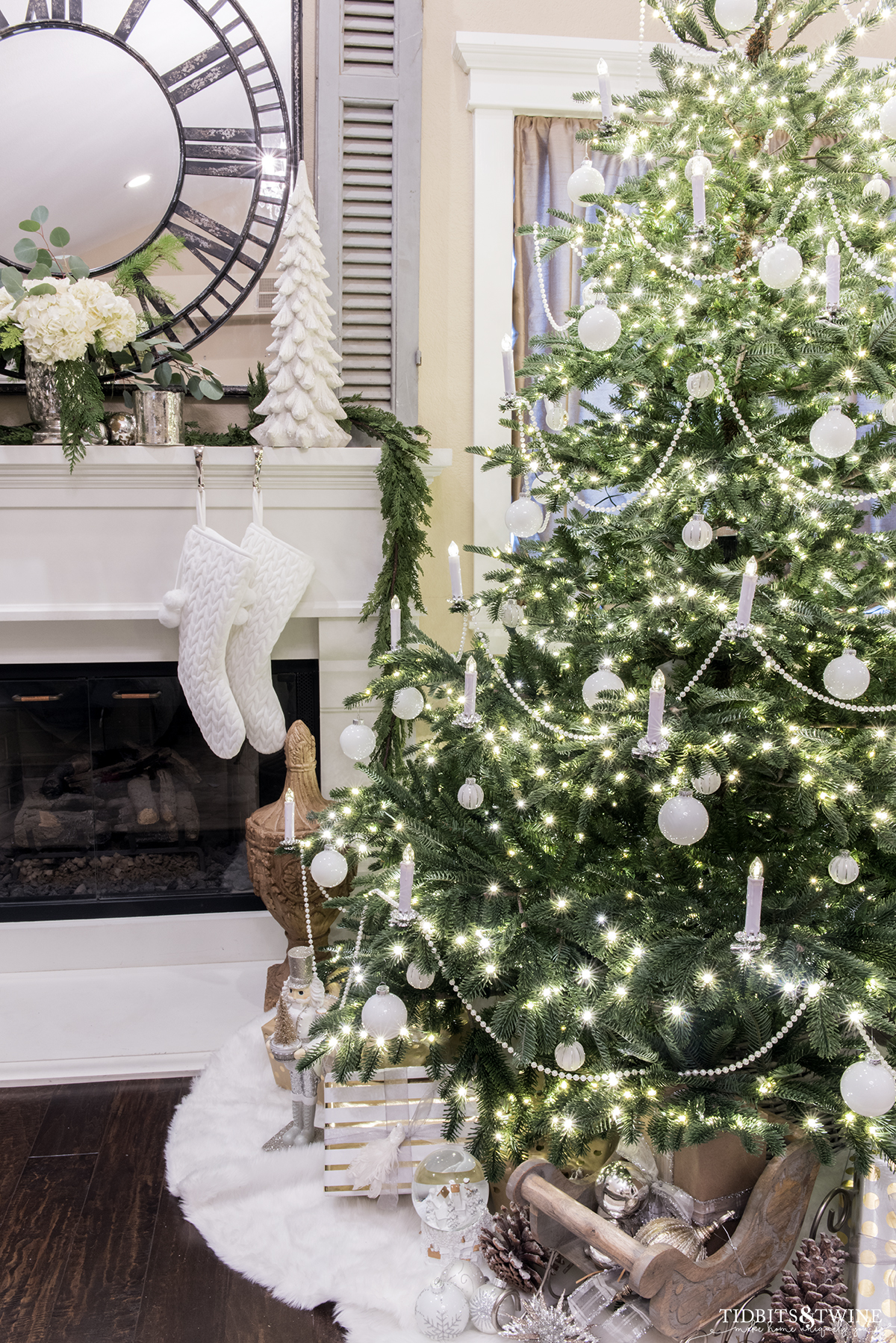 bedroom with european fir christmas tree decorated with white ornaments and candles next to a fireplace with blue shutters above mantel