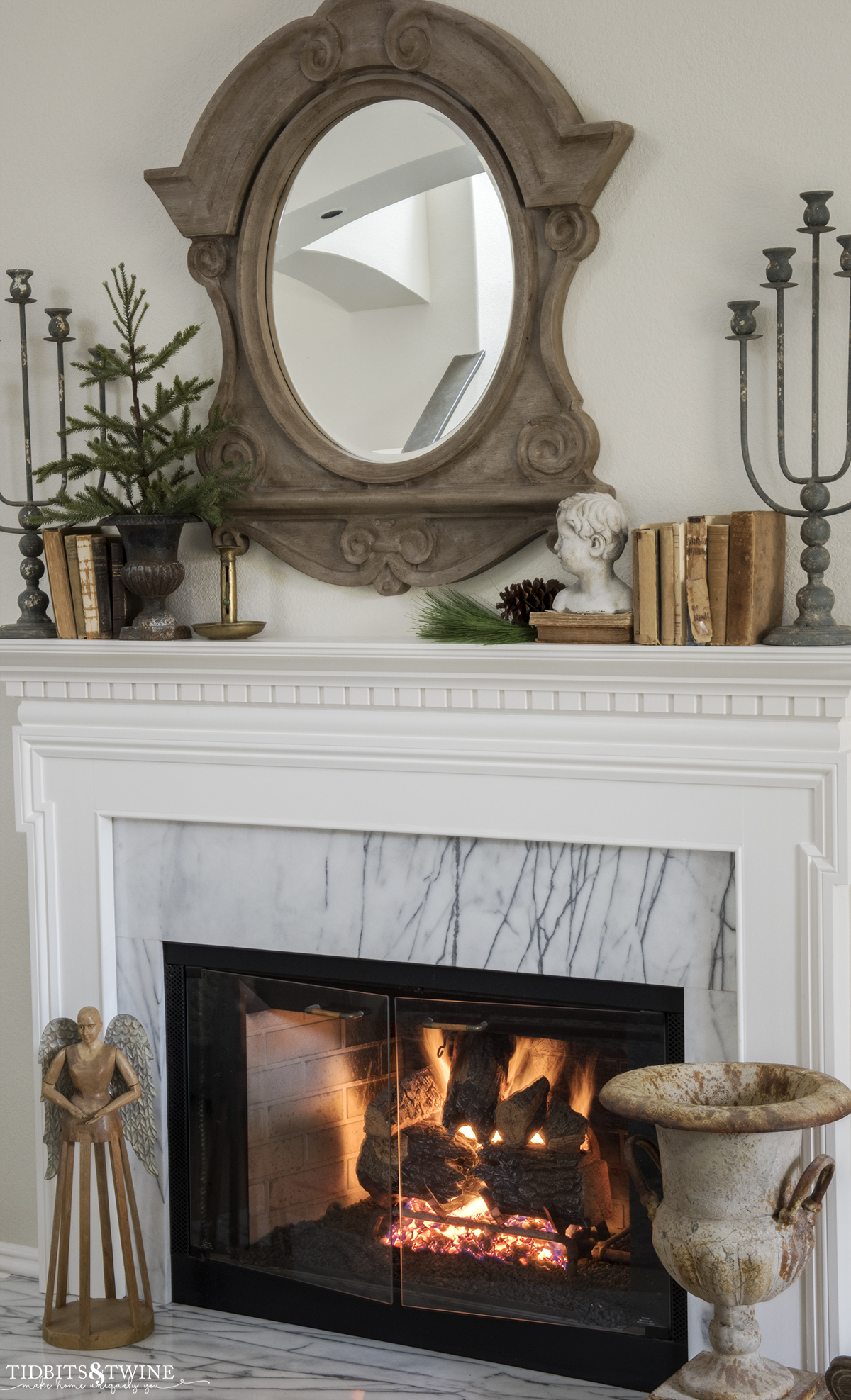 white and marble fireplace decorated for winter with evergreens and vintage books